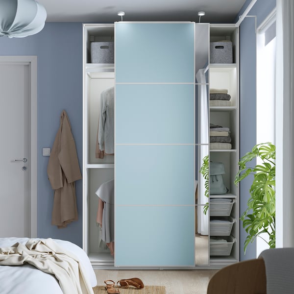 Bedroom with light blue PAX wardrobe featuring sliding doors, hanging clothes, folded towels, baskets, and a plant.