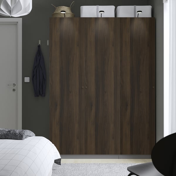 Modern bedroom with large, dark wood PAX wardrobe, white bed, dark carpet, hanging hat, and blue sweater.