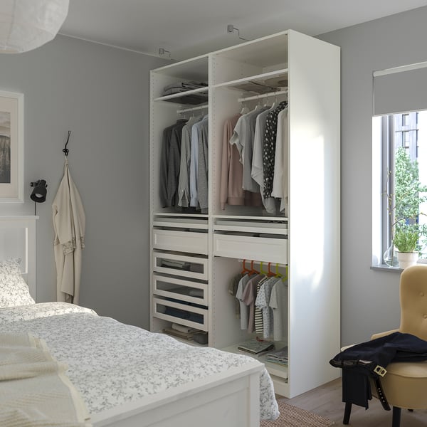 Organised bedroom with large PAX wardrobe, hanging clothes, drawers, floral bedspread, chair, and coat.