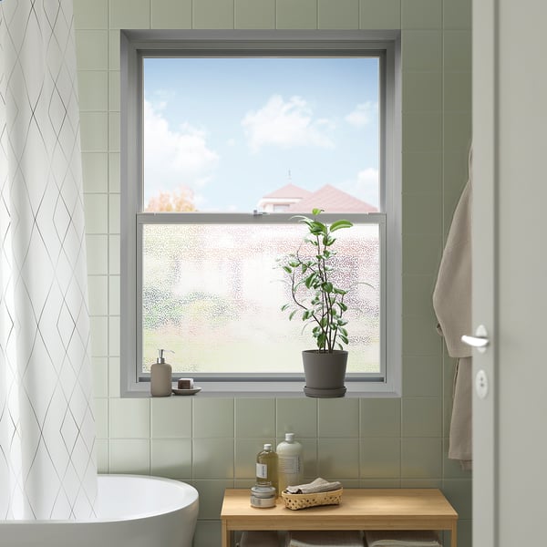 Small bathroom with green tiles, frosted window, and plant.