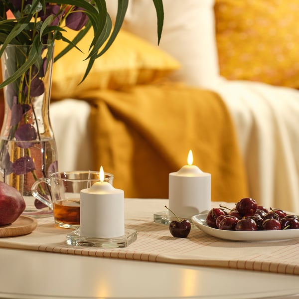 Two SMÅLOM candles; one in lantern, one alone. Surrounded by cherries, flowers, drink. Beige runner, apple coaster. Medium size.