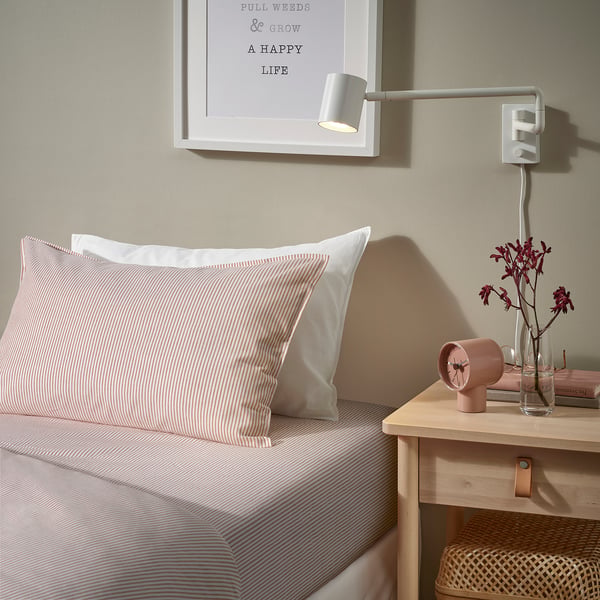 White & peach striped bedding, modern light & bedside table, vase with flowers.