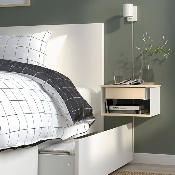 Modern bedroom with wall-mounted bedside table, featuring storage and holding lamp, glass, plants.