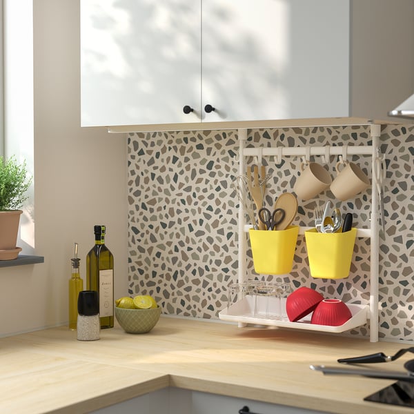 Modern kitchen with beige rack holding utensils, lemons, wine, and candles. Cozy, organized space with patterned wall and natural light.