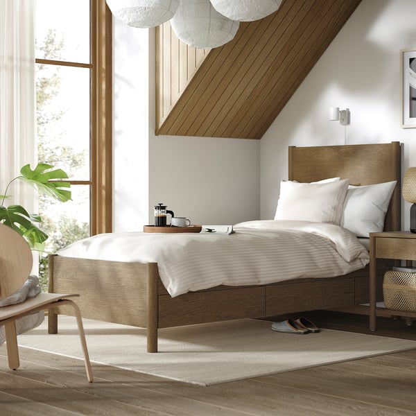 Minimalist bedroom with TONSTAD bed, white linens, wooden bedside table, large window, and plant.