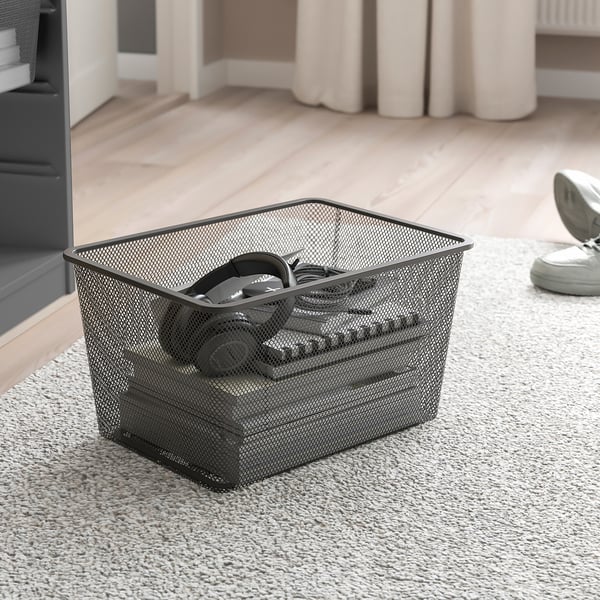 Black mesh storage basket holds headphones on carpeted floor.