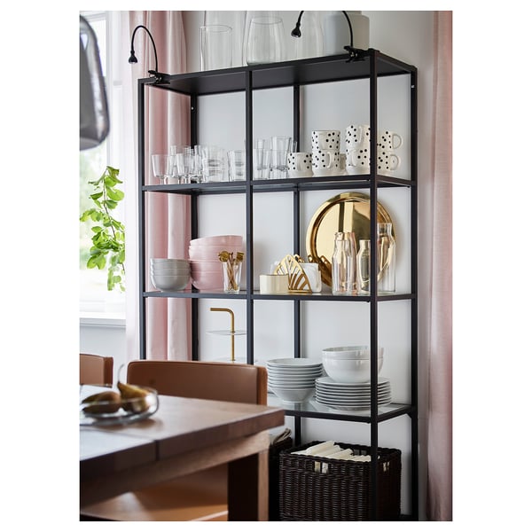 A VITTSJÖ shelving unit with glass shelves, black-brown and black panels, displaying dishes and decor near a dining table.