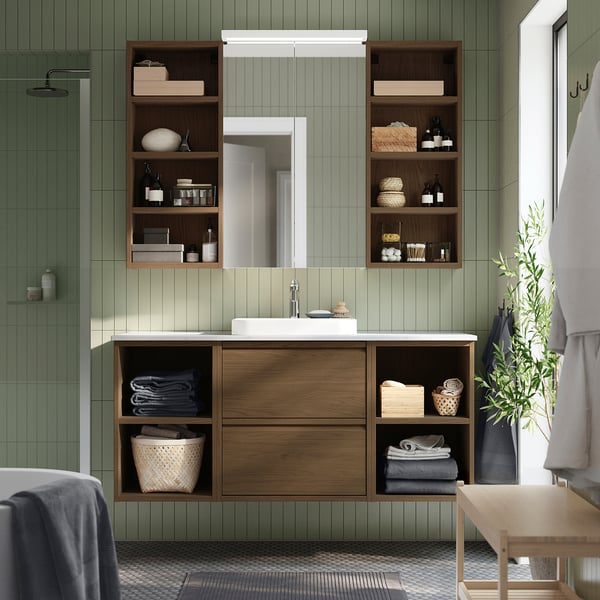 Современная ванная комната с зелёными стенами, дубовым тумбом, раковиной, кладовкой, зеркалом, растением.