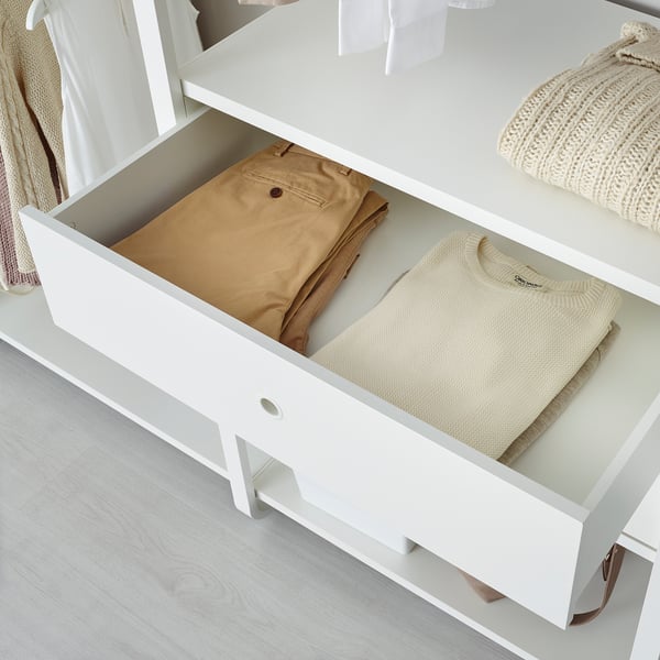 Открытый белый ящик наполнен аккуратно сложенными коричневыми брюками и легким свитером. Входит в состав складского комплекса ELVARLI.