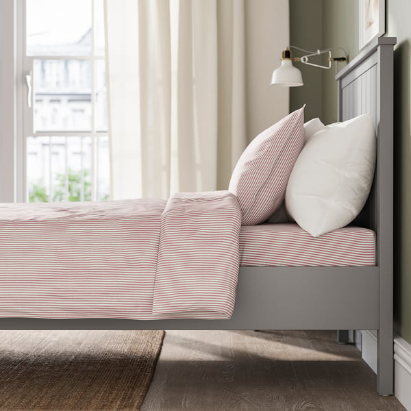 Уютная спальня с серой кроватью GULLABERG , полосатым постельным бельем и мягкими подушками у окна, предлагающая уютное и уютное пространство для сна.