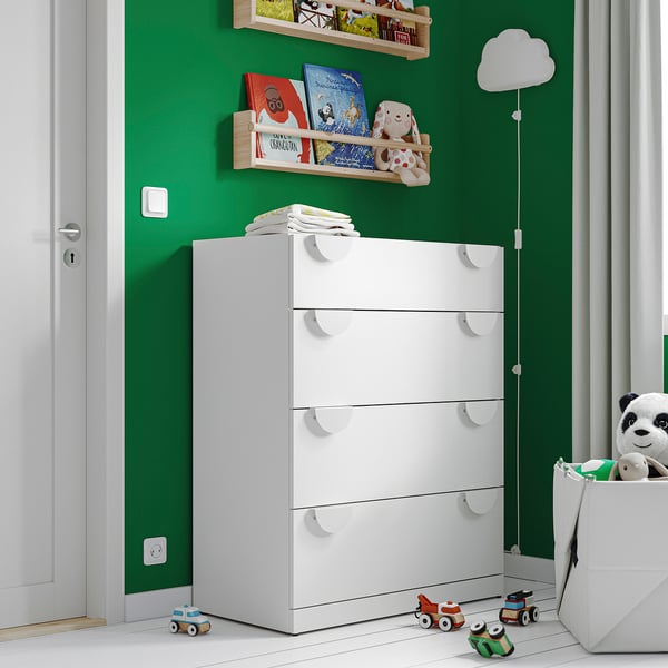 Белый детский комод LASTARE с четырьмя ящиками в грин-комнате, вокруг — игрушки и книги.