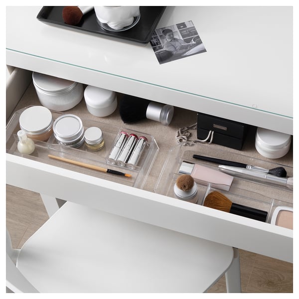 Белый туалетный столик со стеклянной столешницей, широкий ящик для макияжа и украшений. Зеркало сверху, внутри видна упорядоченная косметика.