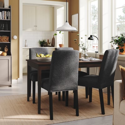 Столовая с темными стульями вокруг деревянного стола, вазой с фруктами. Кухня с белыми шкафами, хорошо освещенная, уютная.