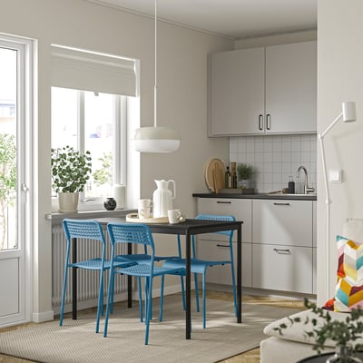 Современная кухня с синими стульями, черным столом, растениями и красочным ковром.