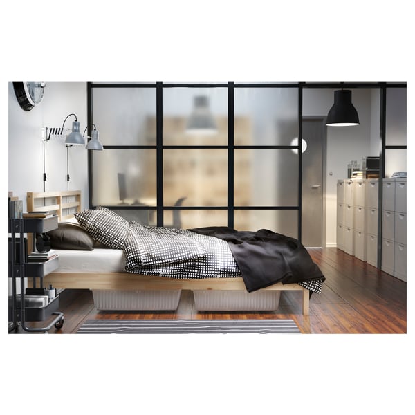 Современная спальня с деревянной кроватью TARVA, черно-белыми постельными принадлежностями, деревянным полом и большими окнами.