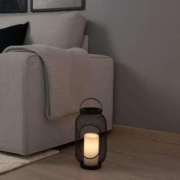 Cosy living space with a grey couch, a beige blanket, and a black lantern with a flickering led candle beside it.