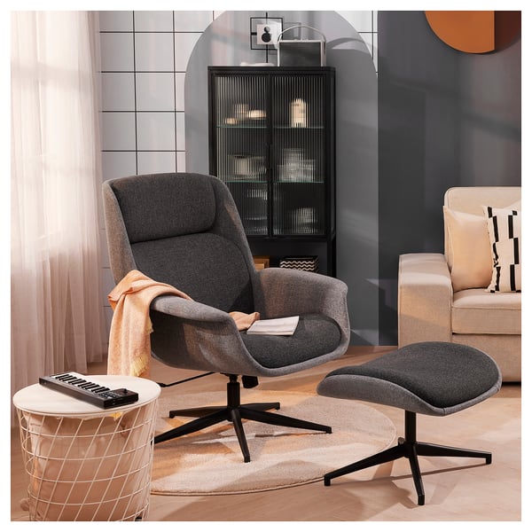 Modern living room with grey ÄLEBY recliner, matching ottoman, and white side table with keyboard. Black cabinet and beige couch in background.