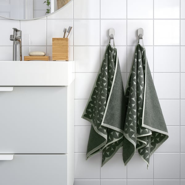 Modern bathroom with two gray-green patterned ÄNGSNEJLIKA towels hanging neatly on hooks, showcasing their intricate design and soft texture.