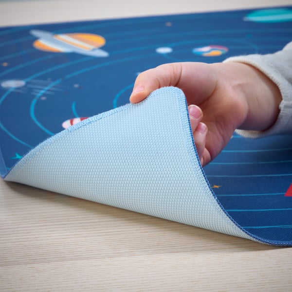 Childs hand lifting blue desk pad with planets, made from recycled polyester, protecting desk from scratches.