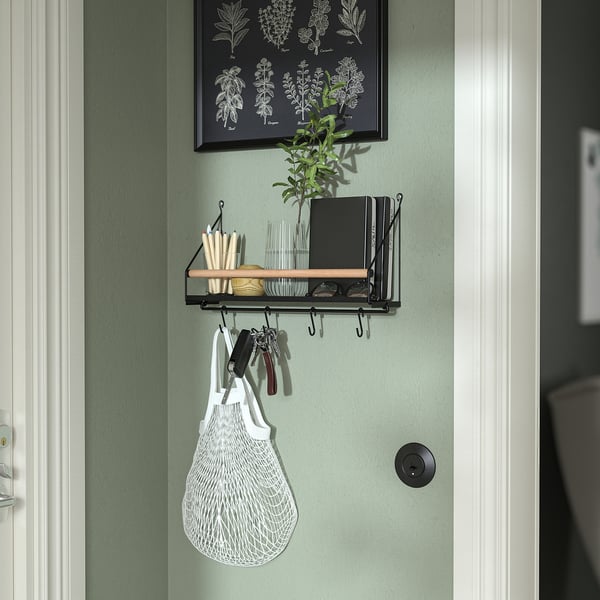 A narrow wall organiser in green with hooks and a shelf. It holds keys, a white bag, and other small items.