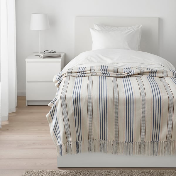 Bedroom with cream/blue striped bed, white pillow, side table lamp.