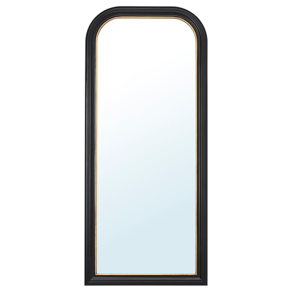 Black-framed mirror with gold trim, arched top, standing against white wall.