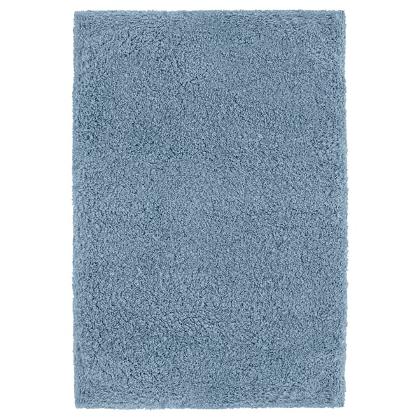 A blue IKEA ALMTJÄRN bath mat, rectangular and soft, made from recycled polyester, offering comfort and absorbency.
