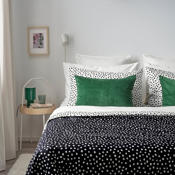 Modern bedroom with ÅSVEIG black-white spotted bedding, green corduroy pillows, small round white side table with green decor, and colourful wall art.