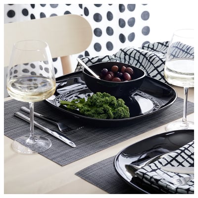 Monochrome table setting with BACKIG black plates, bowls, wine glasses, and cutlery on dark mats.