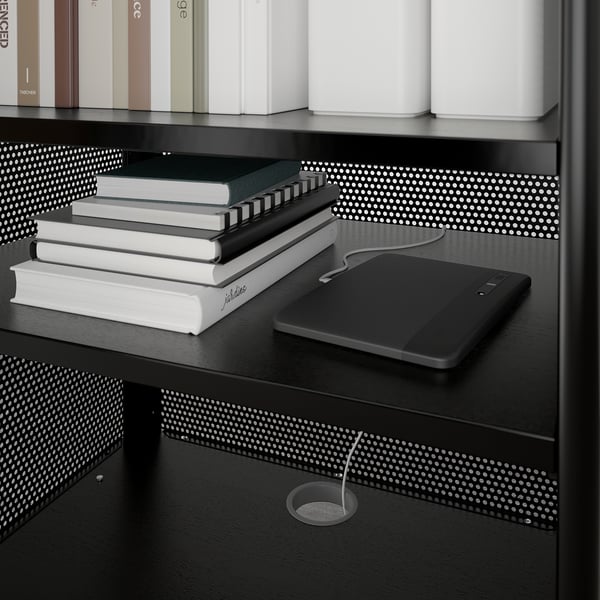 Black bookshelf with adjustable shelves, stack of books, laptop, and cord management grommet.