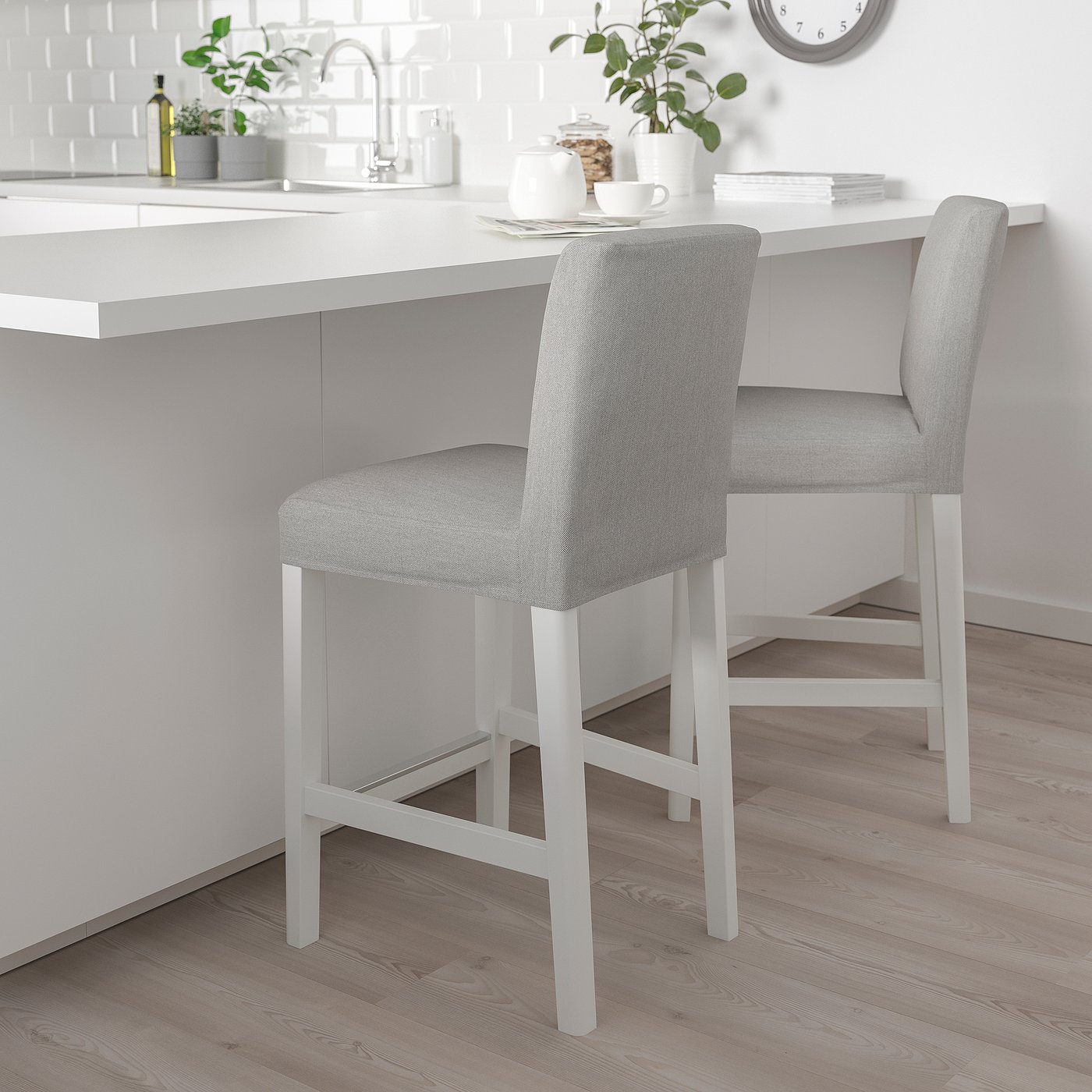 Two grey BERGMUND bar stools beside white kitchen island, offering cushioned comfort with white legs, small in size.