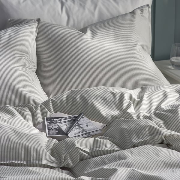 A neatly made bed with a striped duvet cover, pillows, and a black and white book. The fabric looks soft and high-quality.