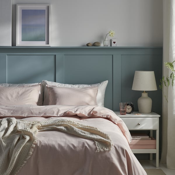 Cosy bedroom with BERGPALM light pink striped duvet, teal headboard, and white bedside table with lamp and clock.