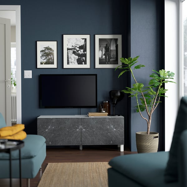 Modern living room with BESTÅ grey tv bench, flat screen, decor, plant, & blue chairs.