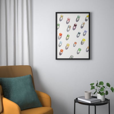 Framed art BILD above yellow armchair, colourful pebbles, books, mug, plant.