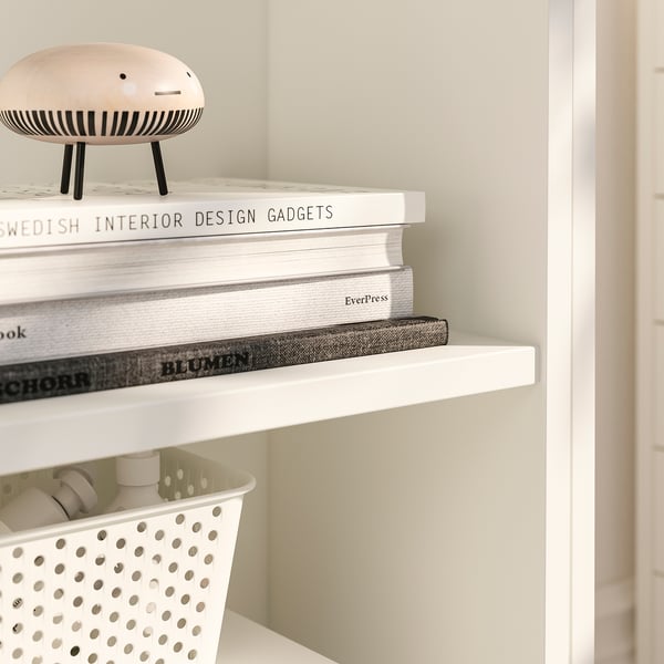 Books neatly stacked on white shelves, top item is unique decor piece.