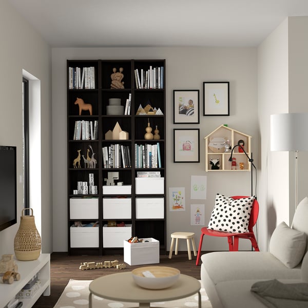 Modern living room with black BILLY bookcase holding books and toys, against light walls with art.