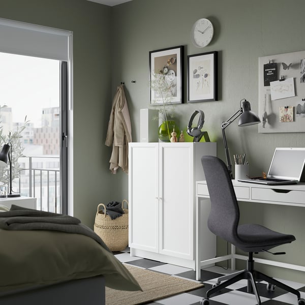 Well-organized home office with BILLY white bookcase, grey chair, wooden floor lamp, and green wall.