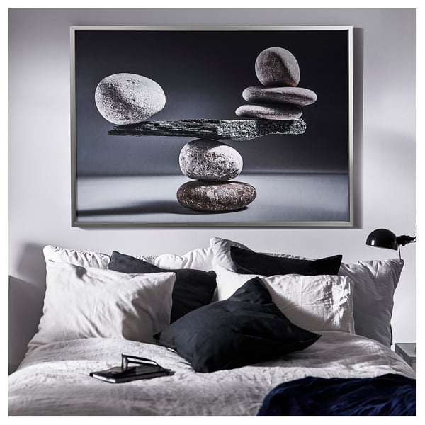 Minimalist bedroom with large stone art, white bedding, blue blanket, black lamp.