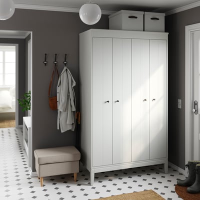Small room with grey walls, white wardrobe, black & white tile floor. Grey bench, coat hooks, and hanging coats, bags.
