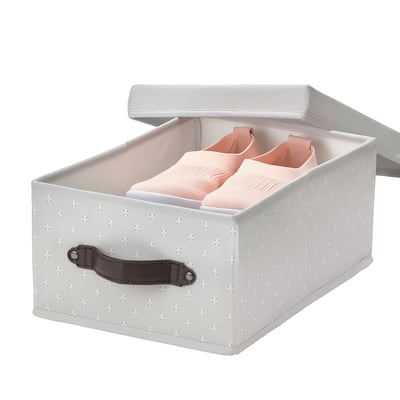 A grey recycled polyester BLÄDDRARE storage box with white floral pattern, featuring a leather-like handle and containing folded pastel pink clothes.