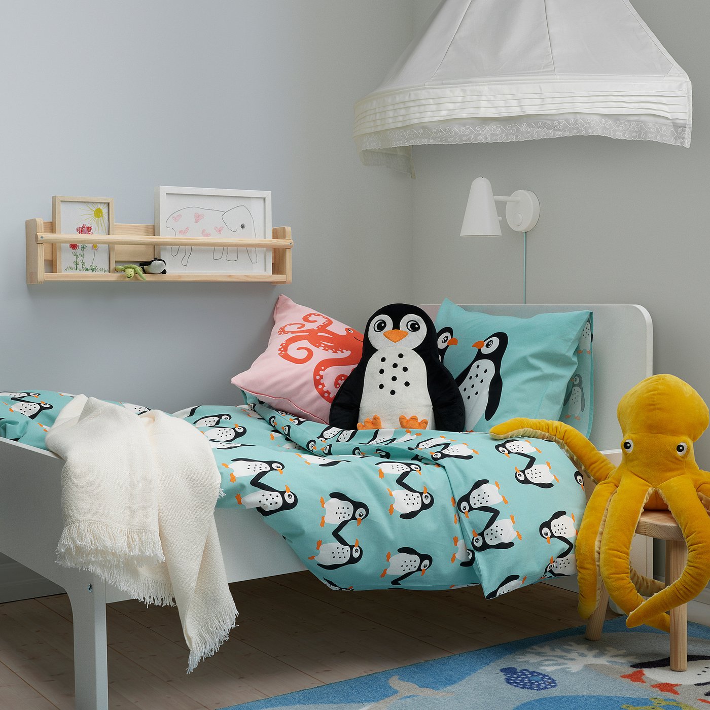 Blue penguin bedding with octopus toy & white canopy in kids room.