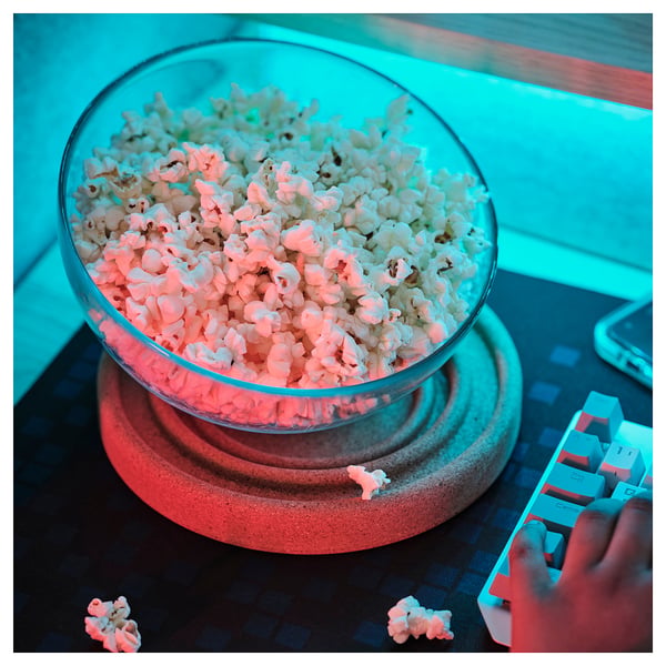 Large bowl of popcorn sits on a smart coaster, reducing spill risk. A hand holds a lego-style toy beside it.