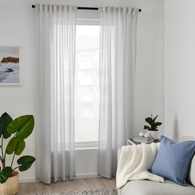 Bright living room with white BYMOTT curtains, a blue pillow, green plants, and a large window allowing natural light to fill the space.