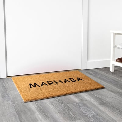 Welcome mat with marhaba on natural fibre by door.