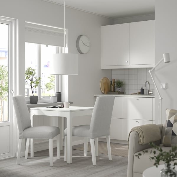 Minimalist kitchen with EKEDALEN table, chairs, and cabinets. Clock, plants, and lamp above.
