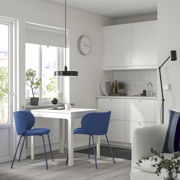Modern kitchen with white cabinets, blue chairs, and a round clock.