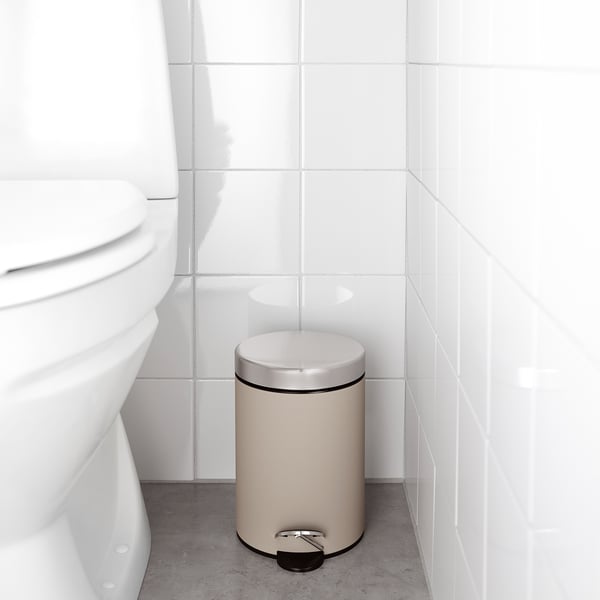 Beige bathroom rubbish can with foot pedal and handle, next to toilet.
