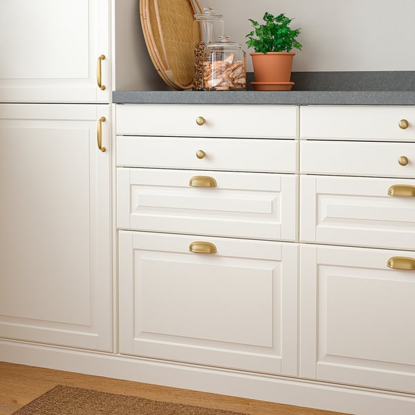 White kitchen cabinets with brass handles and a countertop displaying a pot and jars.
