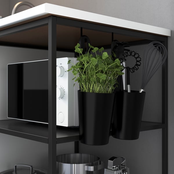 Black shelf with green plants, microwave, and whisk.